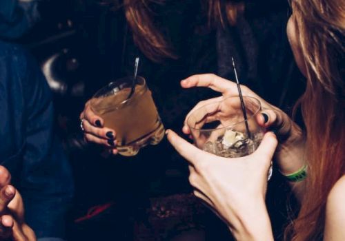 People are enjoying drinks and having a good time, holding cocktails, and smiling or talking to each other in a lively, social setting.