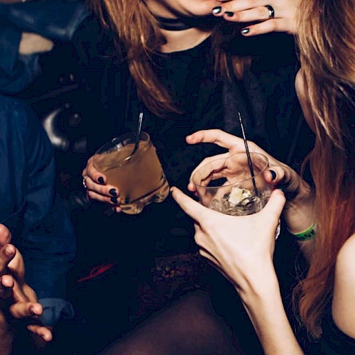 People are enjoying drinks and having a good time, holding cocktails, and smiling or talking to each other in a lively, social setting.