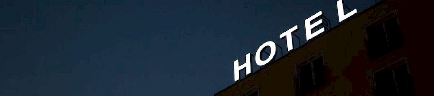 A building with a large "HOTEL" sign is lit up at night, though part of the sign's last letter is out, displaying "HOTEL" against a dark sky.