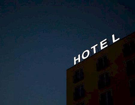 A building with a large "HOTEL" sign is lit up at night, though part of the sign's last letter is out, displaying "HOTEL" against a dark sky.