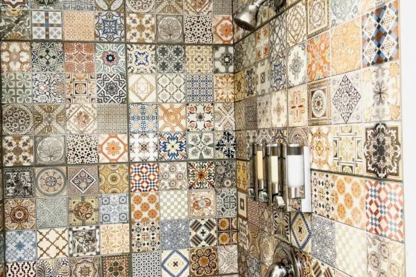 The image shows a shower area with colorful, intricately patterned tiles, a showerhead, and built-in soap dispensers mounted on the wall.