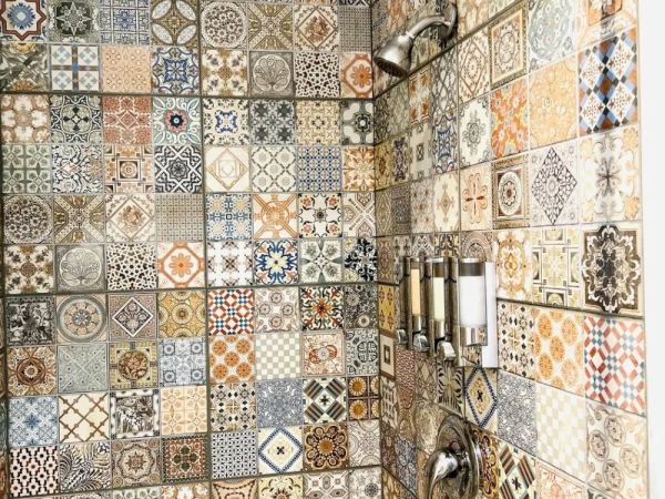 The image shows a shower area with colorful, intricately patterned tiles, a showerhead, and built-in soap dispensers mounted on the wall.