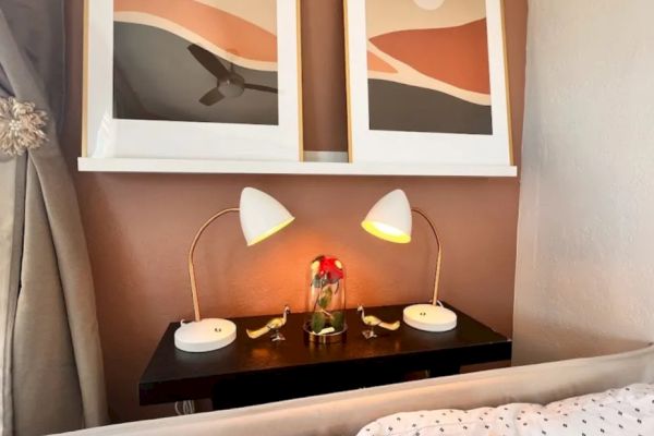 A cozy bedroom setup with two abstract art pieces, matching bedside lamps, a vase with flowers, a cushioned bed, and polka-dot bed sheets.