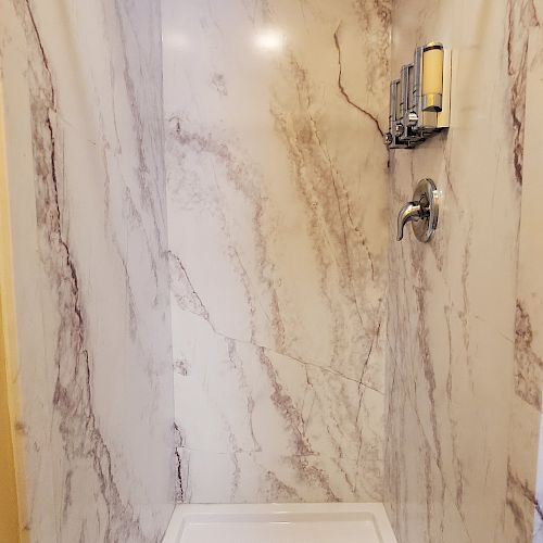 A modern shower area with marble-patterned walls, a showerhead, a soap dish, and a drain on the white shower floor, creating a clean look.