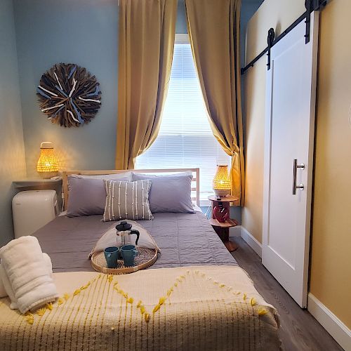 A cozy bedroom with a neatly made bed, two bedside lamps, and decorative wall items, including a woven piece and circular art. Ending the sentence.