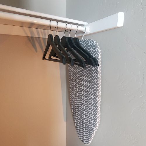 A closet with several black hangers and an ironing board covered with a patterned fabric, hung on the closet rod.