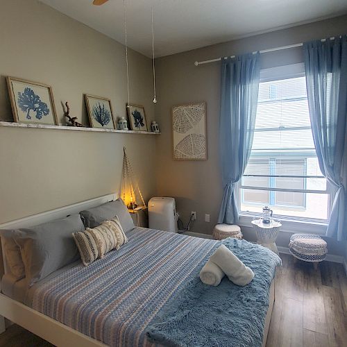 A cozy bedroom with a striped bed, decorated shelf, candles, and curtains over a window. The room has a modern yet warm atmosphere.