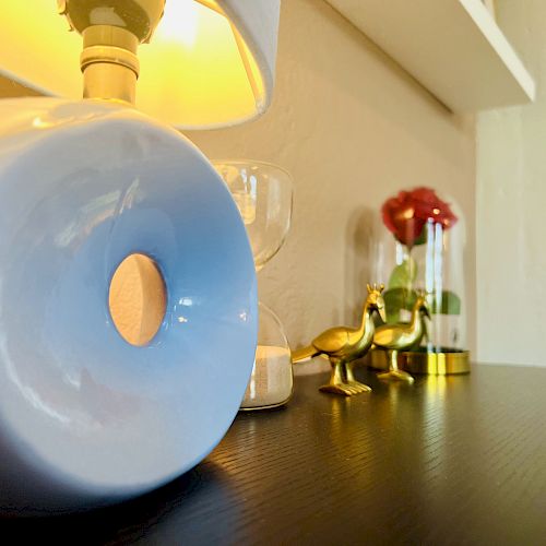 A lamp, an hourglass, a small golden bird ornament, and a decorative red rose on a dark tabletop.