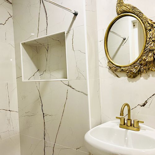 A bathroom with marble tiles, a white sink with a gold faucet, and a gold-framed mirror with an ornate design.