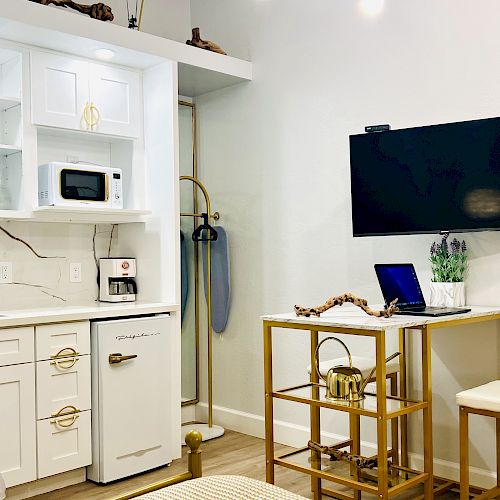 A compact kitchen with a microwave, sink, and fridge; a small dining area with a high table, bar stool, and a wall-mounted TV.