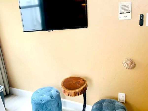 A wall-mounted TV, a thermostat, blue poufs, small wooden tables, and wall decor in a cozy room.