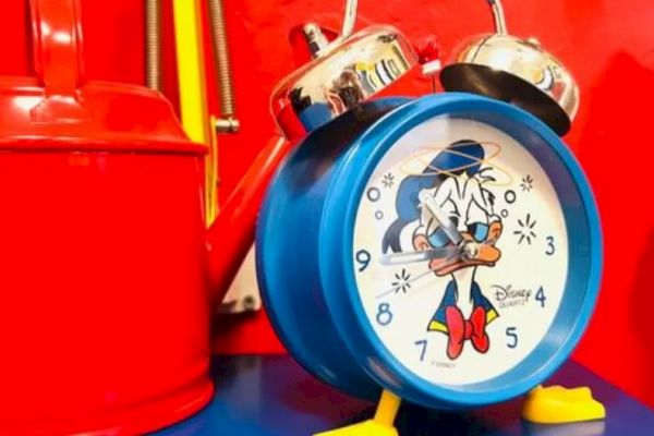 A blue alarm clock with a cartoon character, likely from Disney, next to a red container on a blue surface.