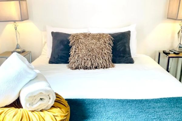 A neatly made bed with decorative pillows, a rolled towel, and lamps on bedside tables. Posters are displayed above the headboard, creating a cozy atmosphere.