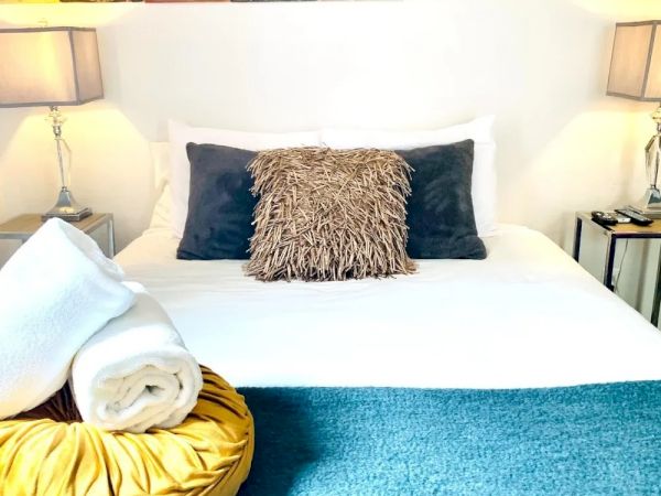 A neatly made bed with decorative pillows, a rolled towel, and lamps on bedside tables. Posters are displayed above the headboard, creating a cozy atmosphere.