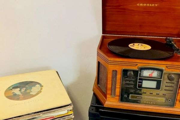 A vintage Crosley record player is playing a vinyl record, with a stack of vinyl records placed next to it.