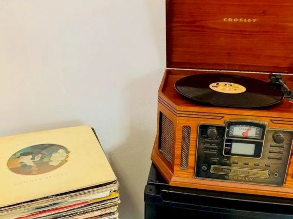 A vintage Crosley record player is playing a vinyl record, with a stack of vinyl records placed next to it.
