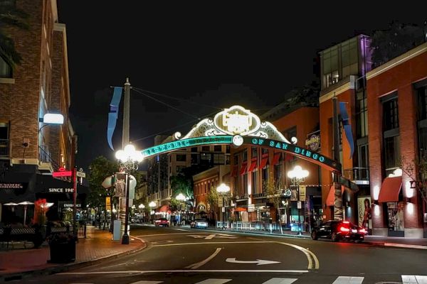 The image shows a nighttime urban street scene with an illuminated arch, buildings, streetlights, and some pedestrians and vehicles.