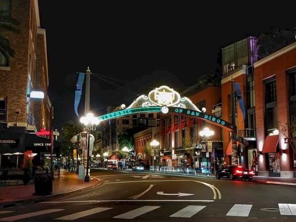The image shows a nighttime urban street scene with an illuminated arch, buildings, streetlights, and some pedestrians and vehicles.