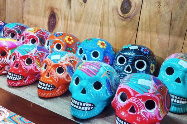 The image shows a row of brightly colored, decorative skulls with intricate patterns, likely used for Day of the Dead celebrations.