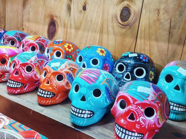 The image shows a row of brightly colored, decorative skulls with intricate patterns, likely used for Day of the Dead celebrations.