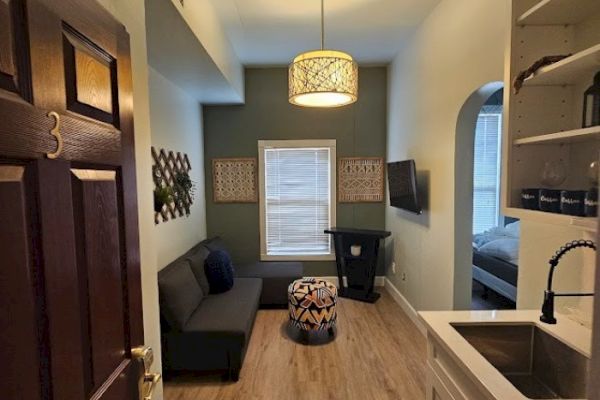 A small, cozy living space with a sofa, ottoman, wall decor, and a sink area, viewed from an open door marked with the number 3.